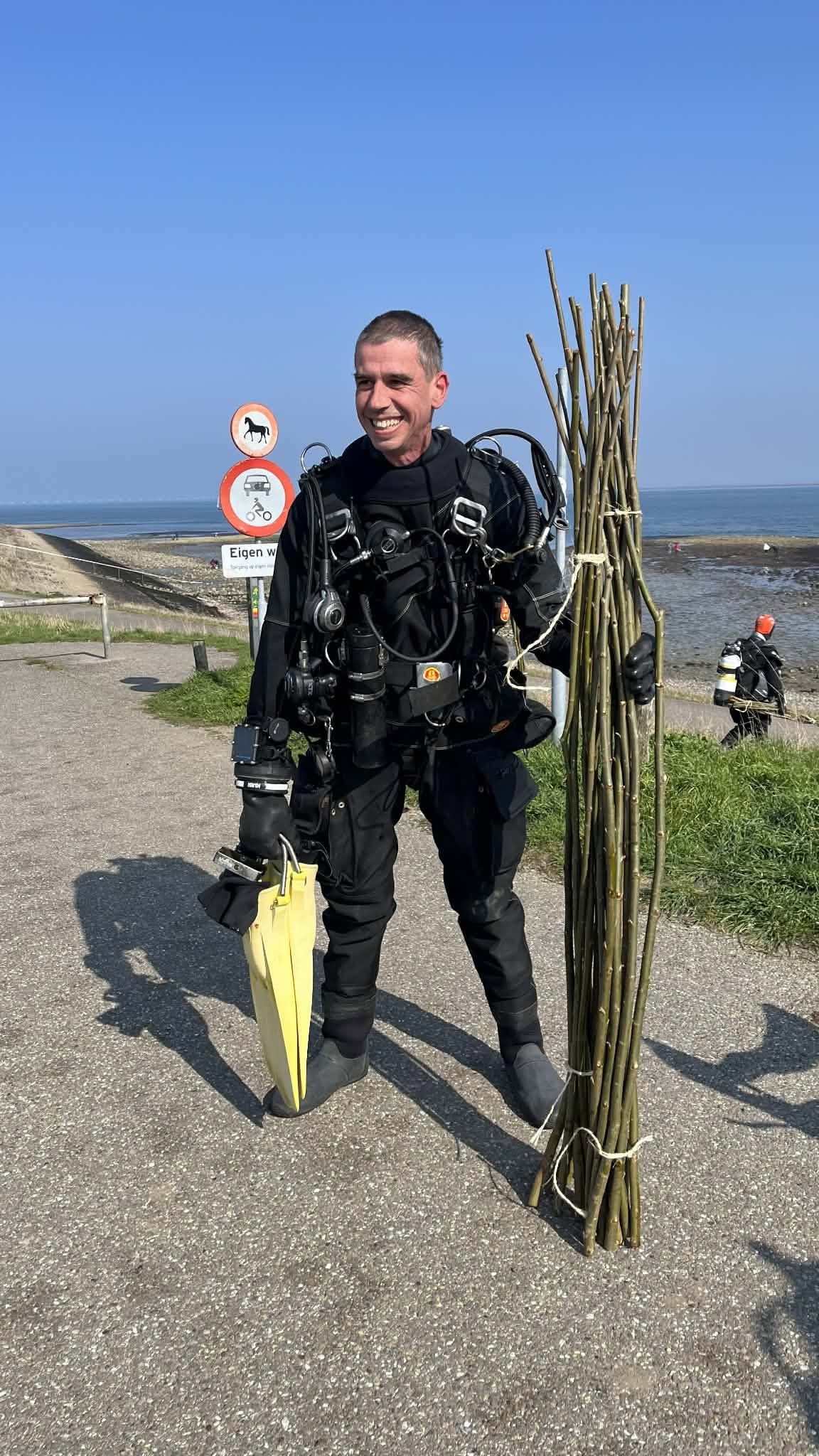 Een duiker met een bundel wilgentakken aan de oever van de Oosterschelde